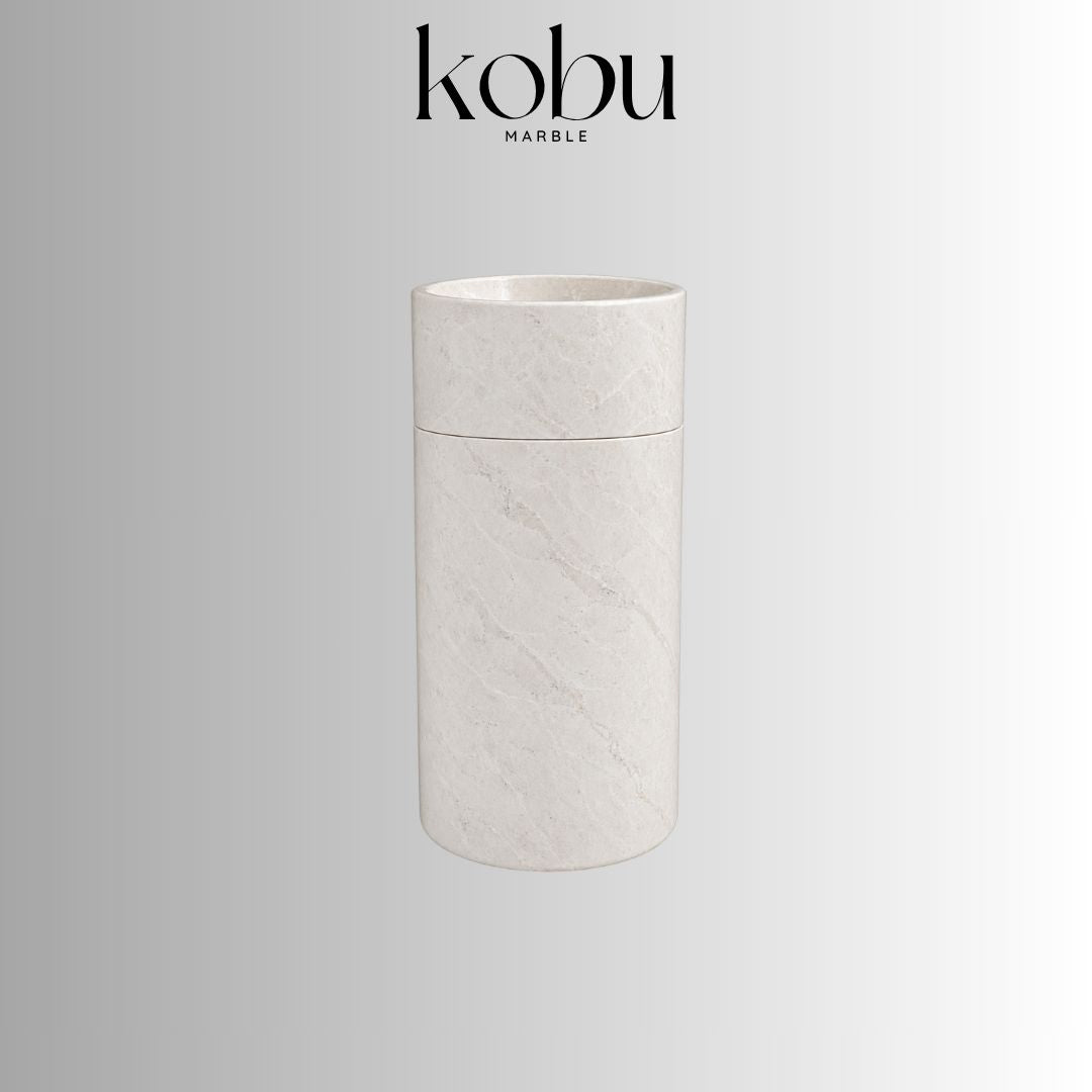 Beige marble cylinder pedestal sink with a round basin, smooth finish, and subtle natural veining